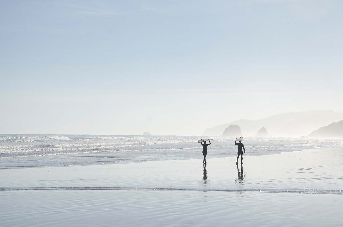 grey two men carrying surfboards near body of water coast