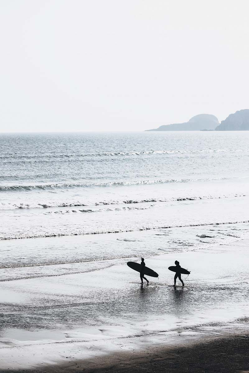 ocean two people carrying surfboards at beach during daytime grey