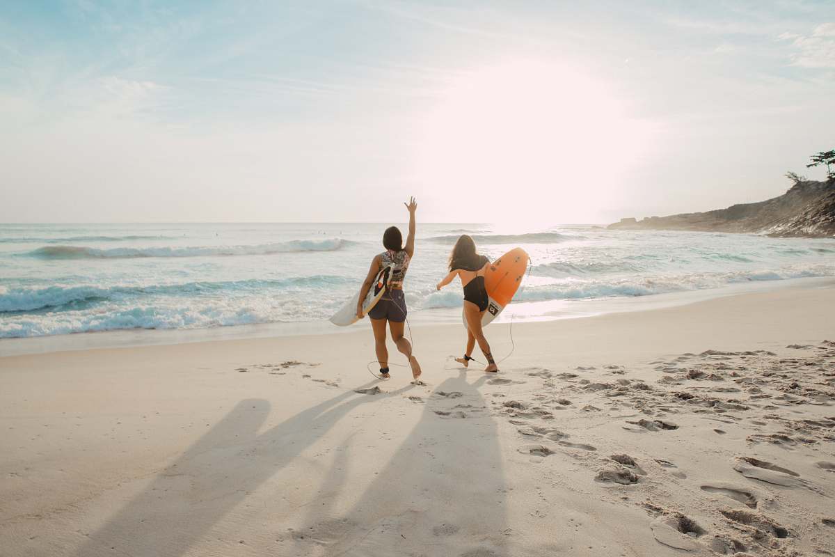 ocean two women walking towards the ocean carrying surfboards during day sea