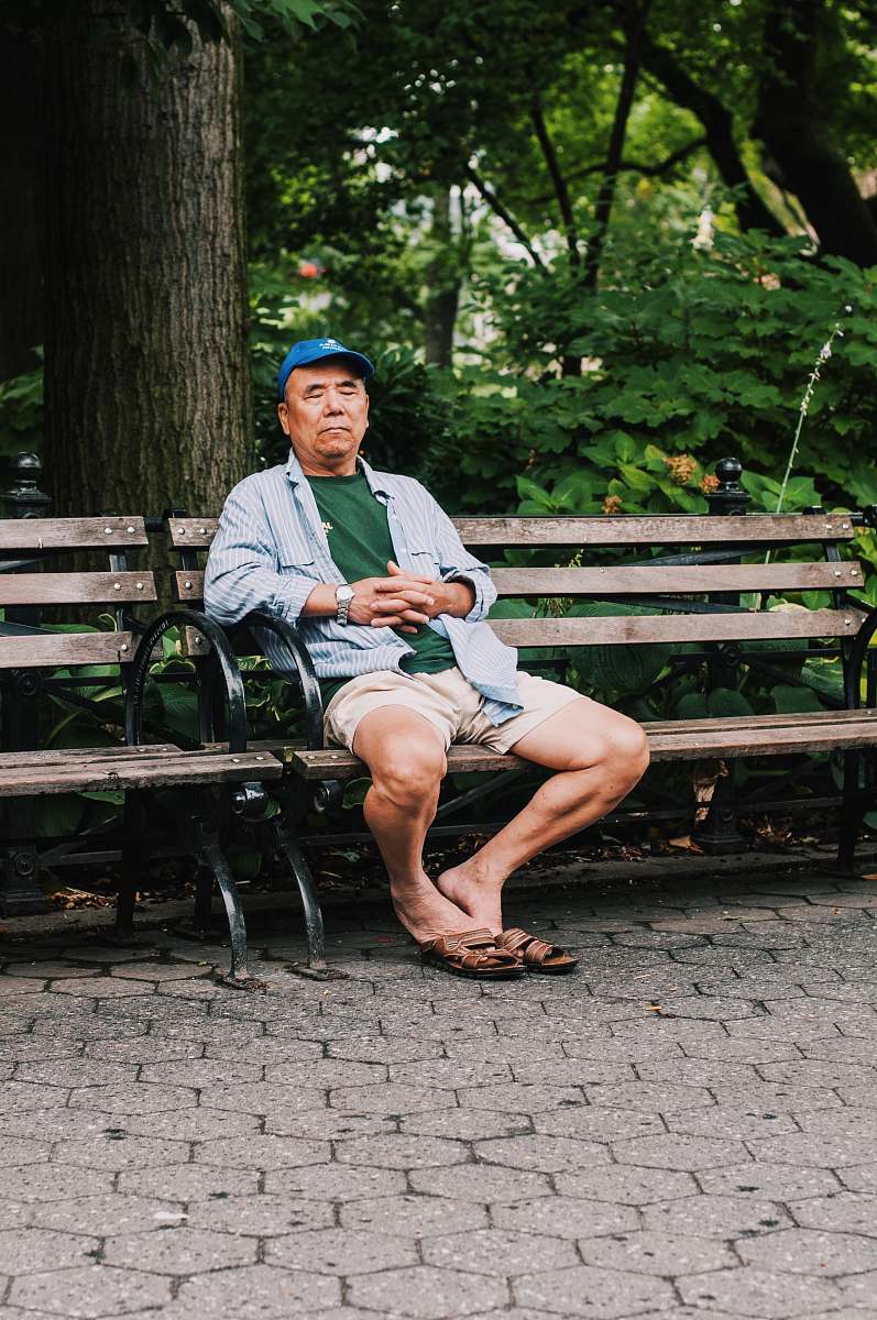human man sitting on bench closing his eyes near trees people