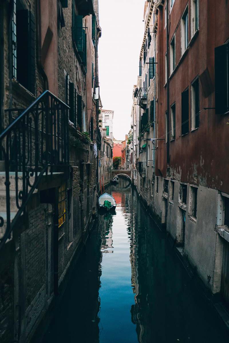 water white boat on canal in between concrete houses building