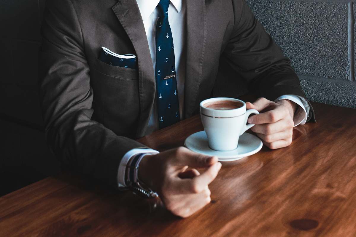 business man holding cup filled with coffee on table hand