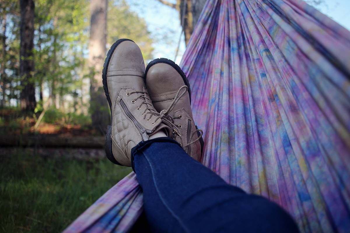 nature person lying on pink and purple hammock surrounded with trees boots