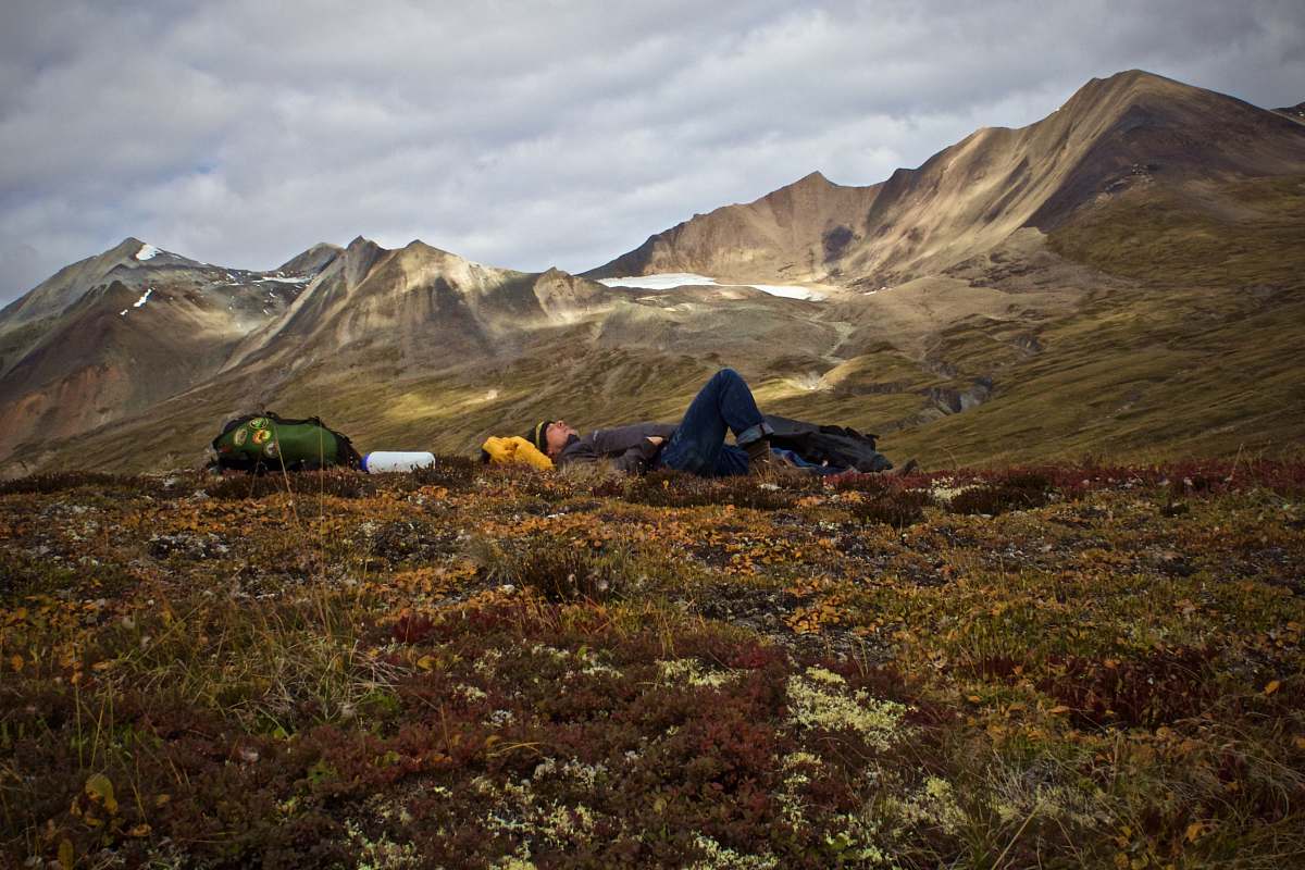 outdoors man lying on plant field near mountains camping