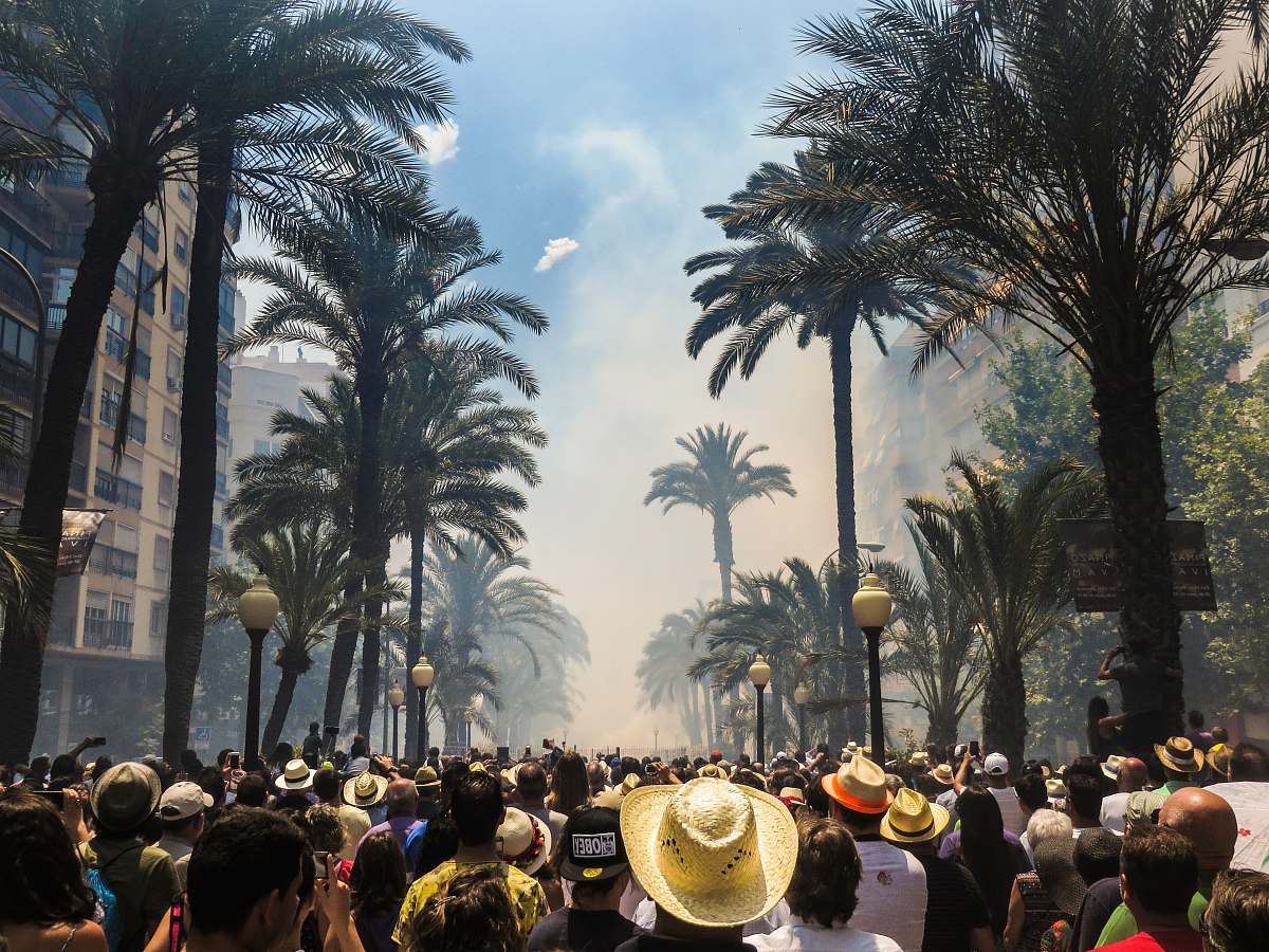 crowd people standing on road between coconut palms surrounded by smoke human