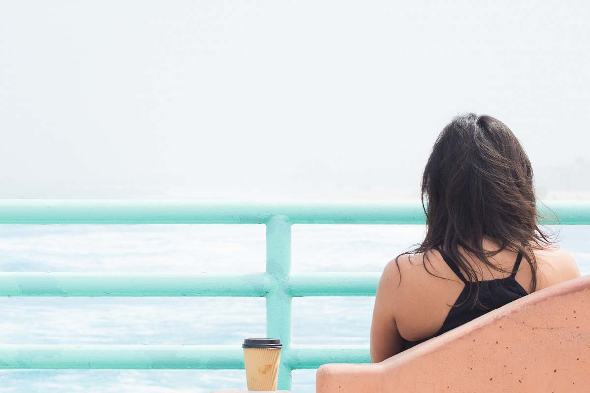 person woman sitting on chair beside cup in front of body of water water