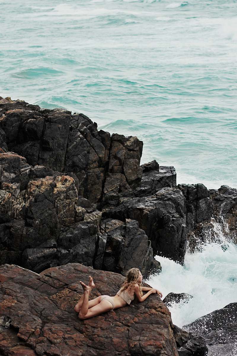 water woman lying on rock formation on seashore bikini