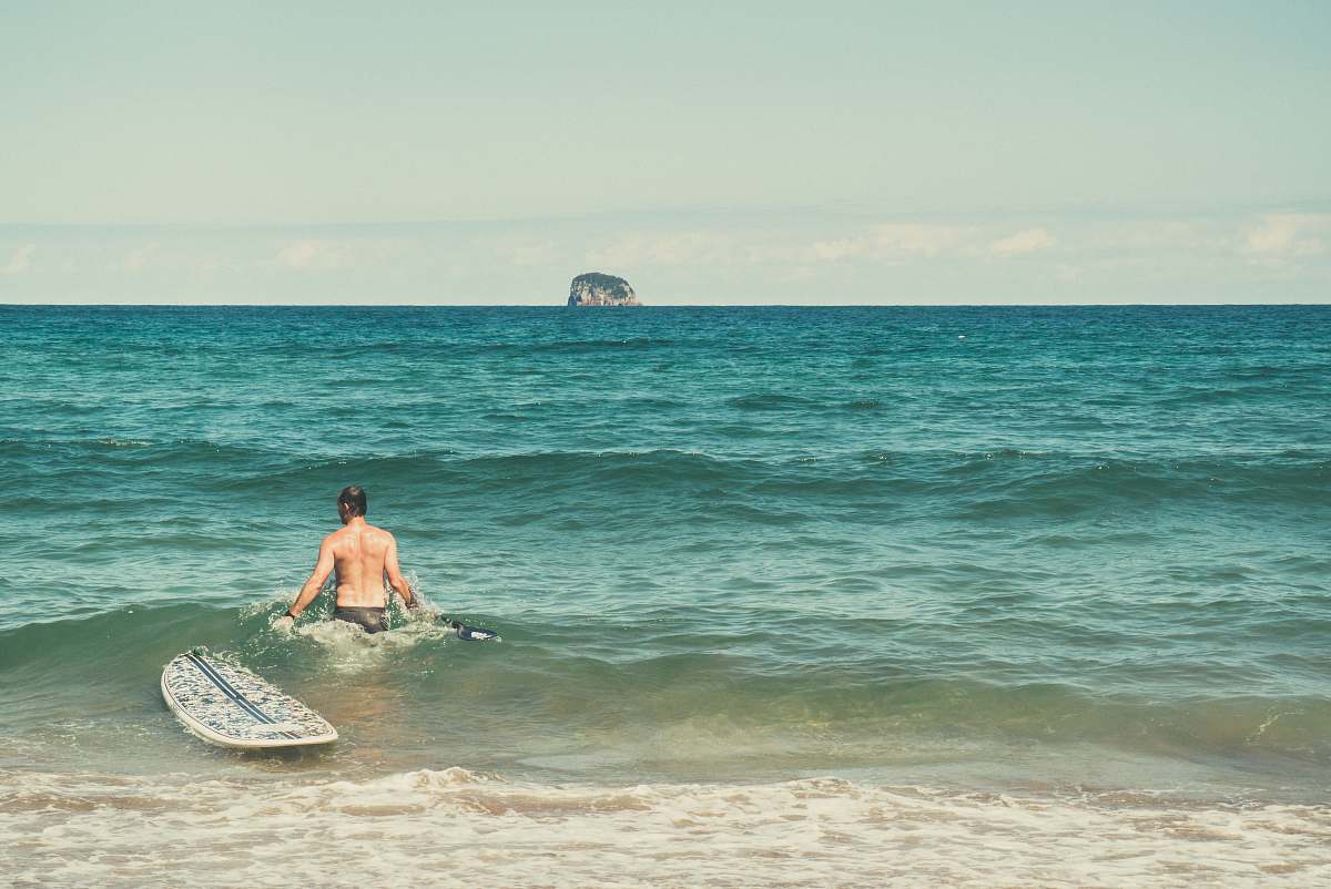 ocean man in water beside surfboard beach