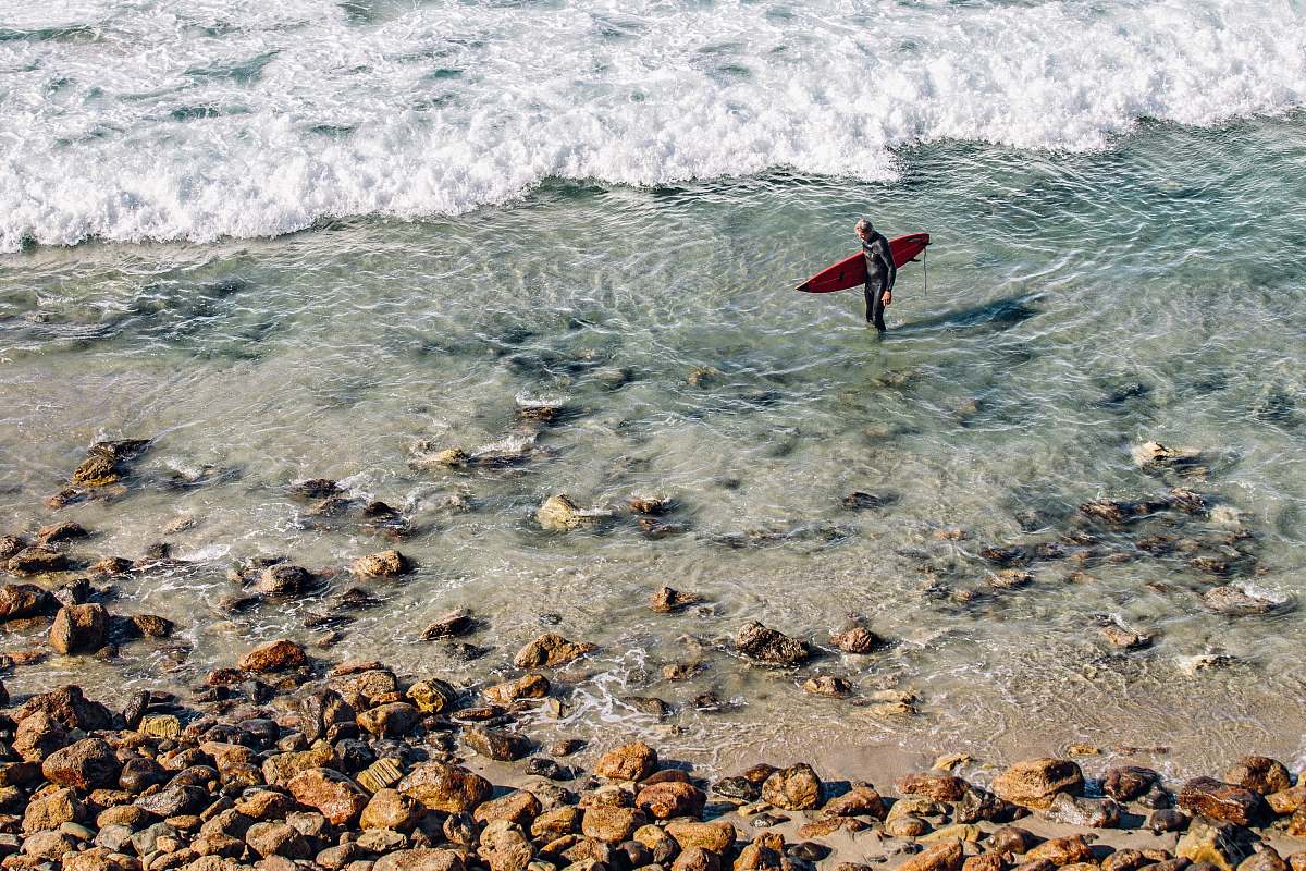 waves people holding red surfboard standing on body of water rocks