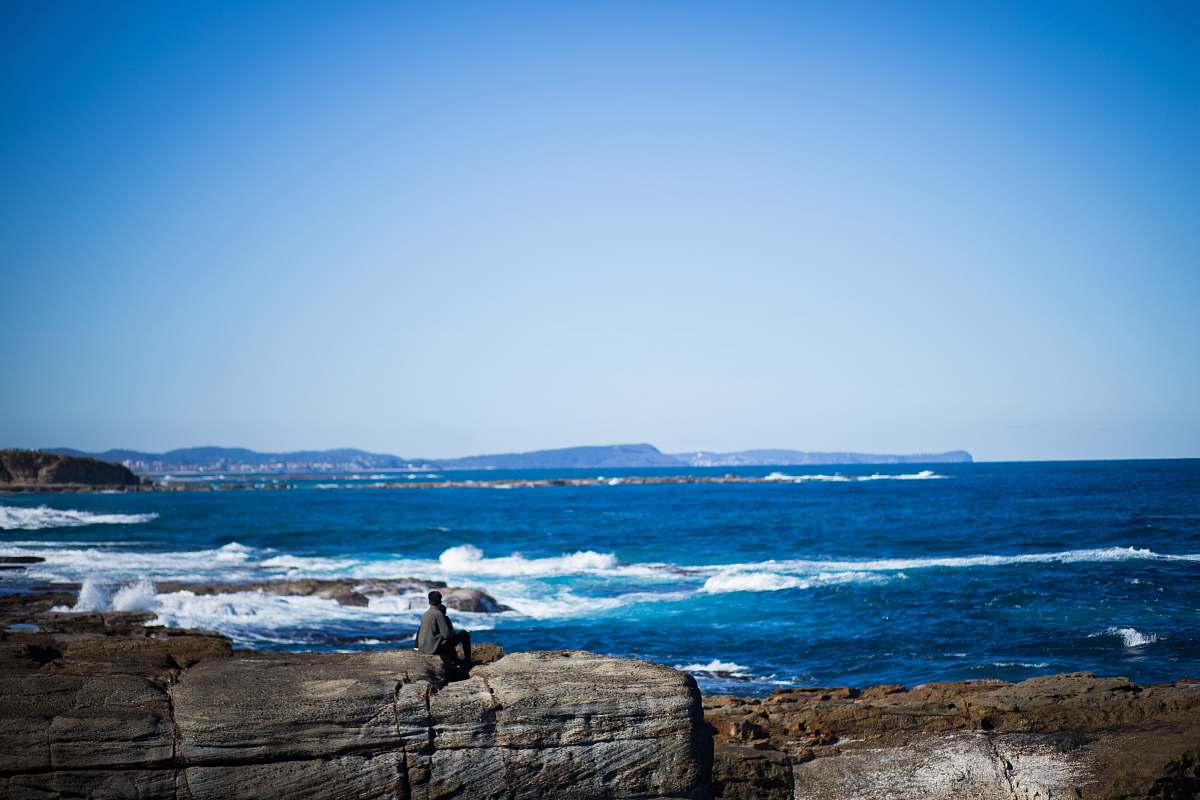 coast man seats on brown stone near sea during daytime nature