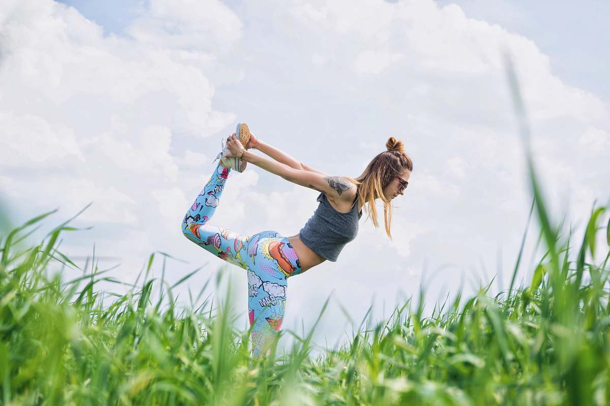 fitness woman standing on left foot while lifting right foot upwards during daytime people