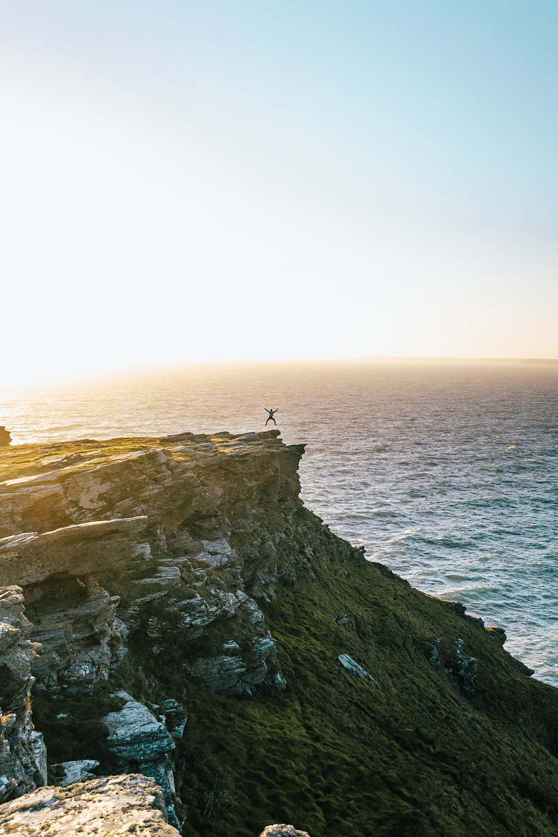 coast man jumping on cliff ocean
