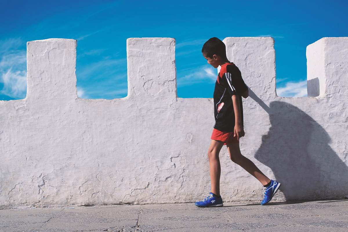 Capture the essence of childhood with this striking image of a young boy walking alongside a pristine white concrete wall. The simple yet captivating backdrop emphasizes the innocence and curiosity of youth, making it ideal for use in projects related to childhood, urban lifestyle, or modern design. Perfect for educational content, blog posts, or advertising campaigns focused on children's products and services.