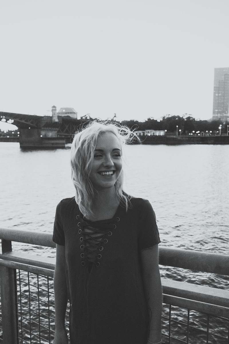 person grayscale photo of smiling woman standing near fence above body of water grey
