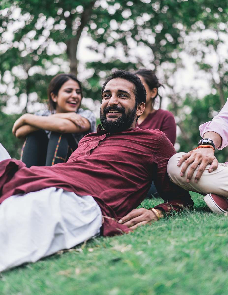 people man in maroon dress shirt lying on green grass field smile