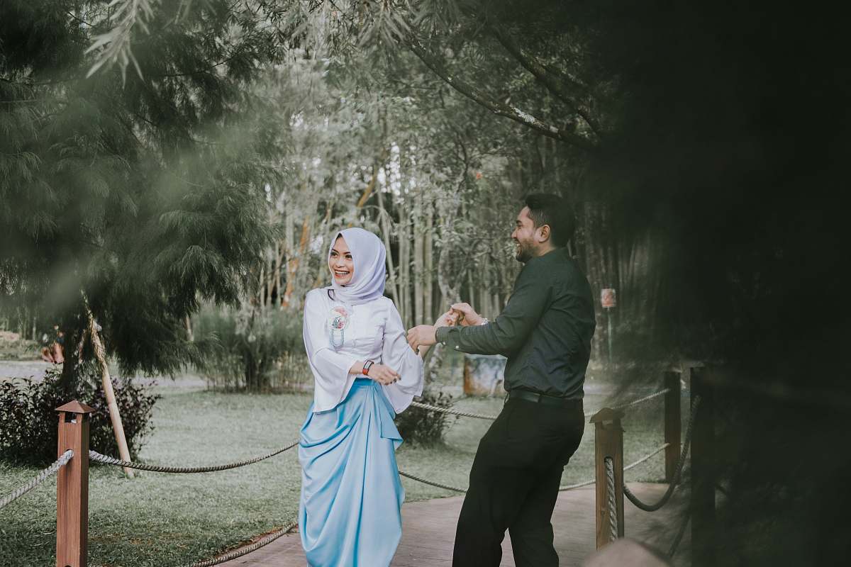 person man smiling looking at woman smiling and standing on bridge near green leaf trees during daytime people