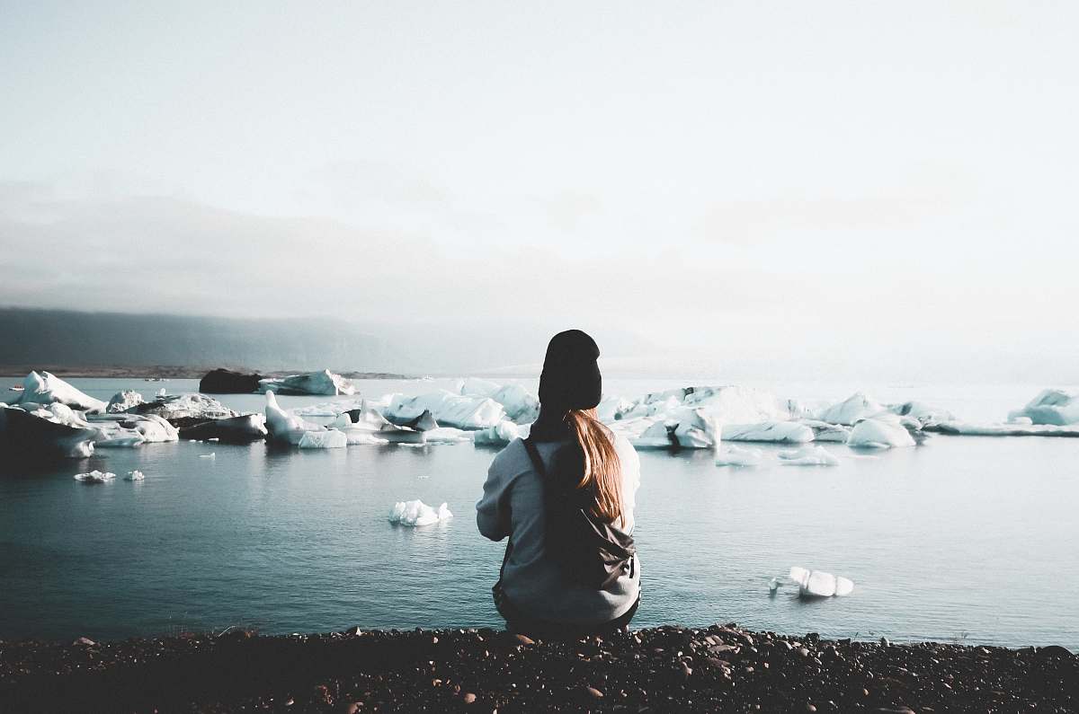 This captivating image features an unknown woman sitting peacefully near a glimmering lake, surrounded by the beauty of nature. The soft ripples of water reflect the surrounding greenery, creating a serene atmosphere perfect for relaxation and contemplation. Ideal for use in wellness blogs, environmental campaigns, or any content that emphasizes tranquility and the connection between humans and nature.
