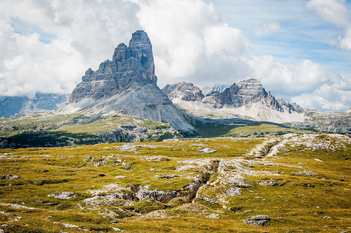 mountain rock formation on wide field grass under cloudy blue sky during daytime landscape