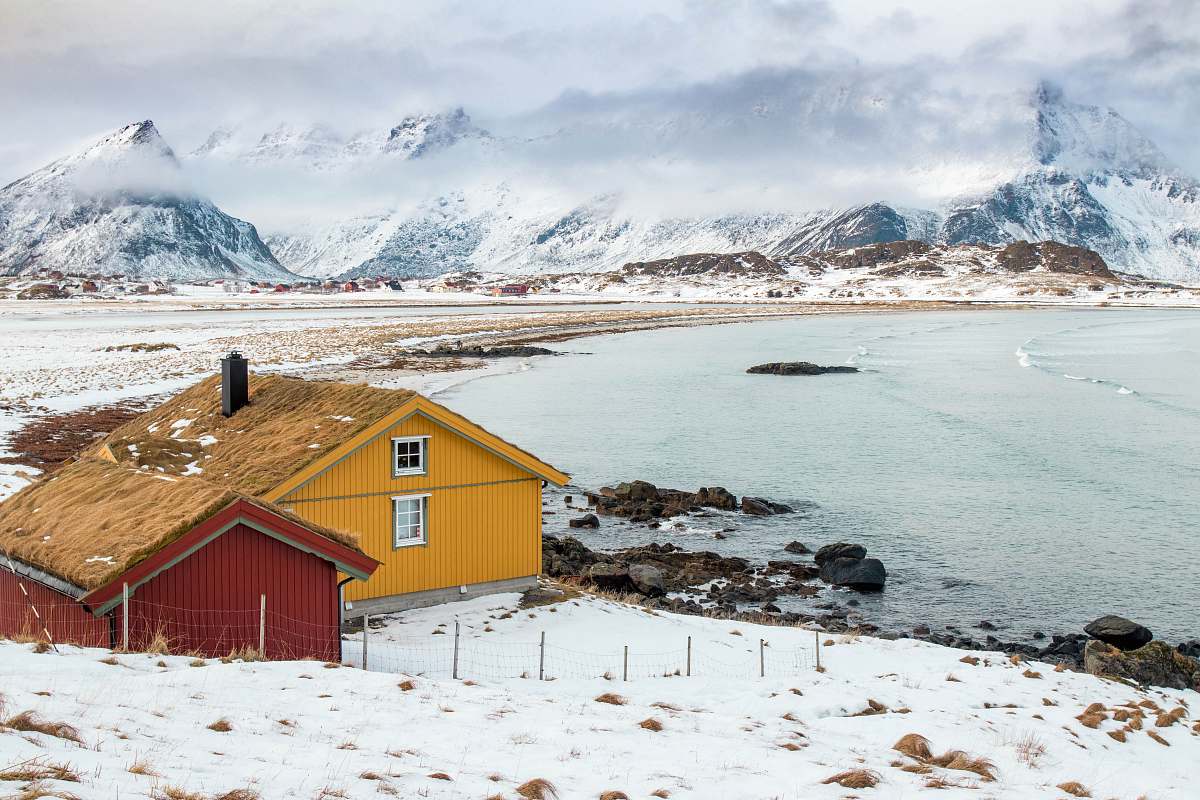 outdoors two houses near body of water across hill at daytime norway