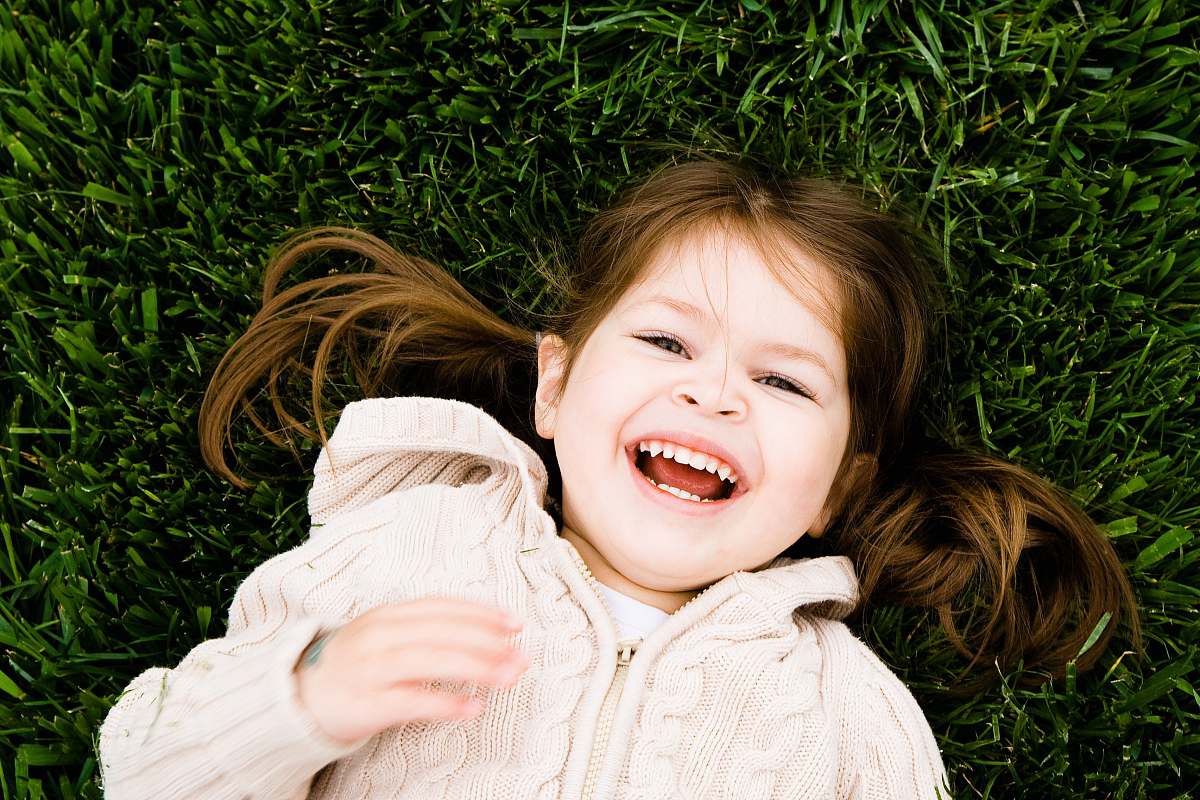 human girl smiling while lying on grass field at daytime person