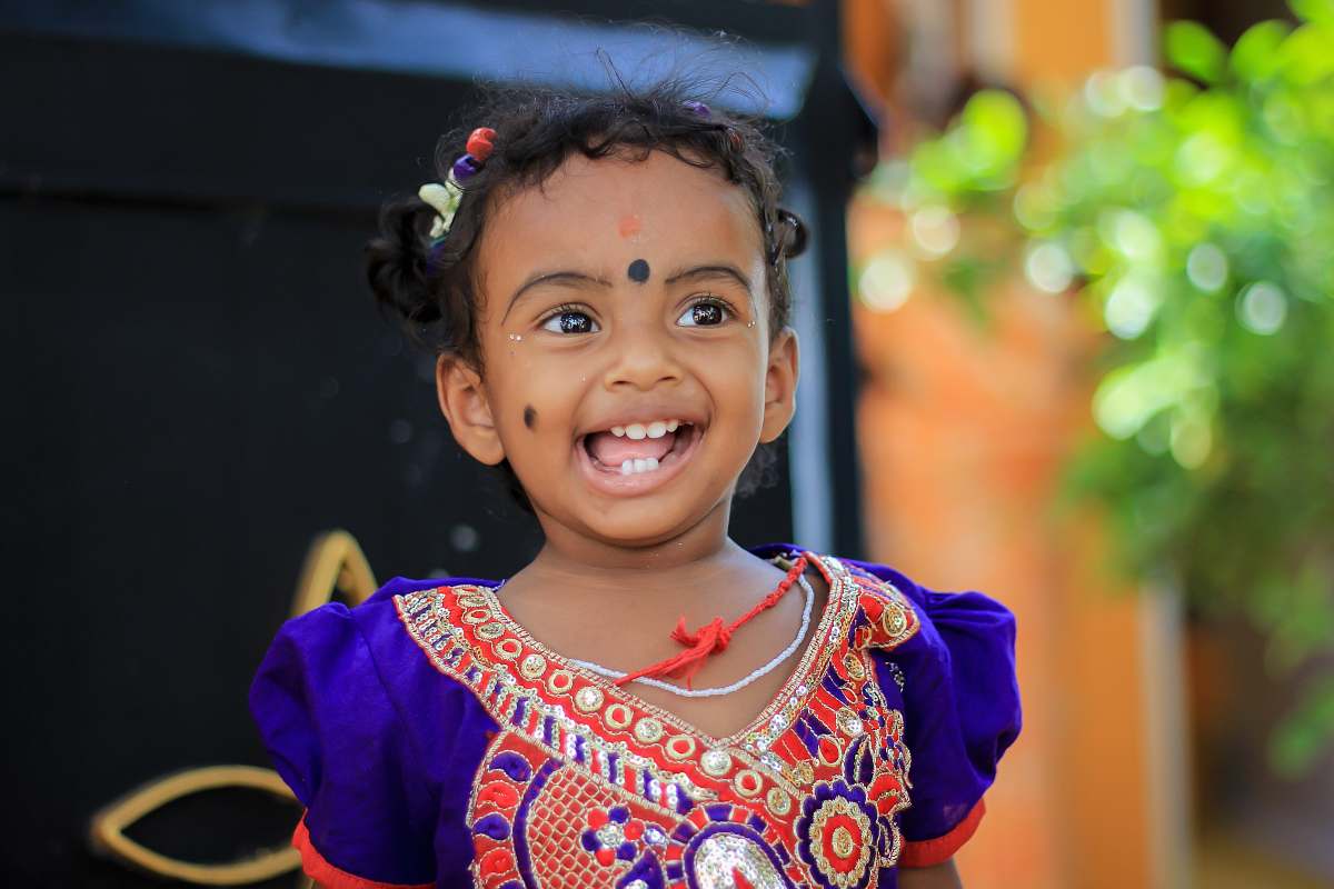 india selective focus photography of girl smiling while standing near plant at daytime girl