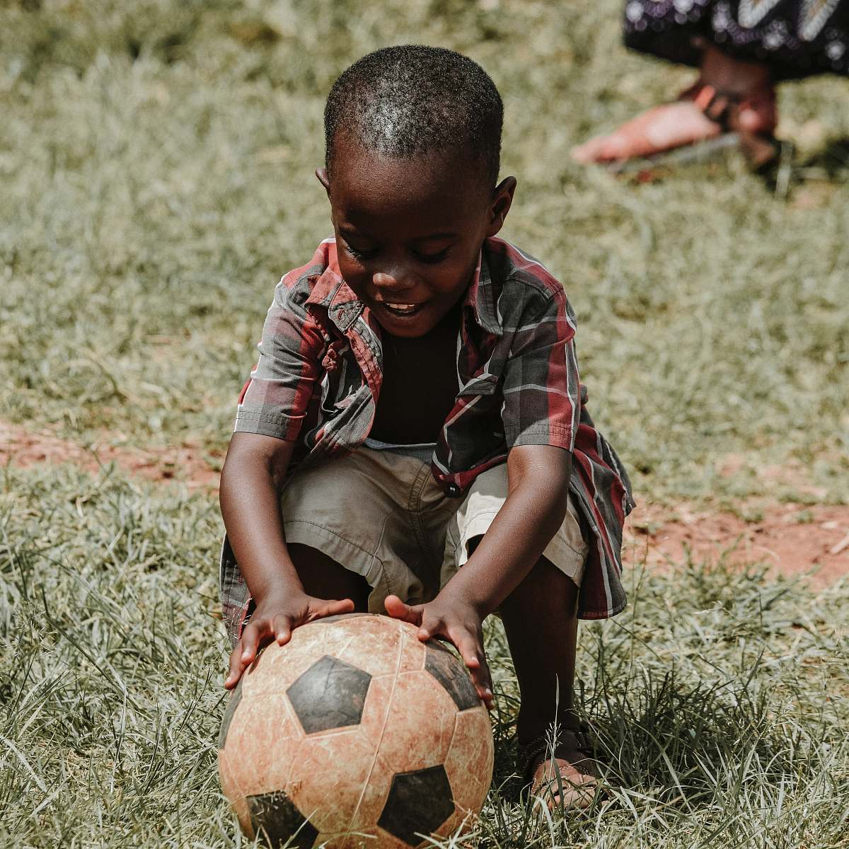 football smiling boy sitting while holding soccer ball at daytime soccer