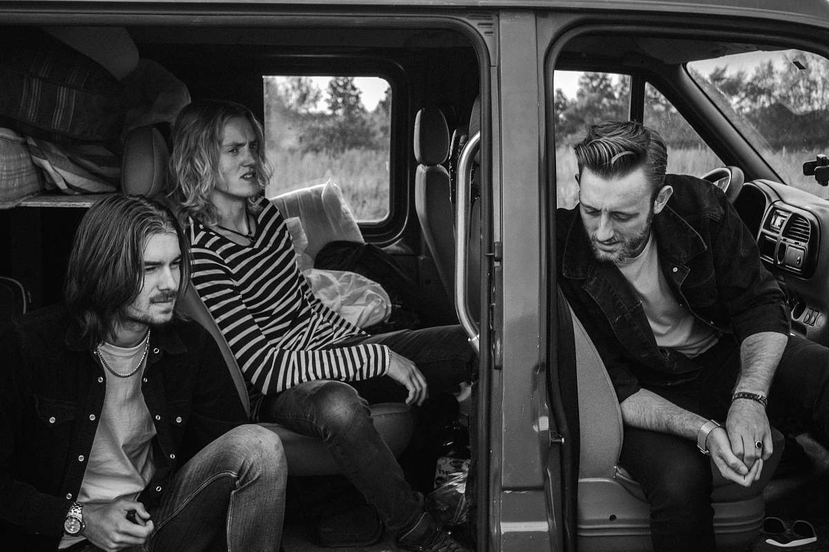 people grayscale photo of three men sitting on vehicle seats black-and-white