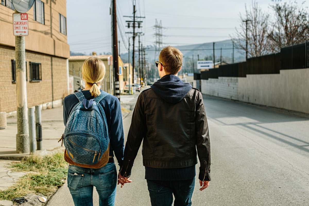 couple man holding hands of woman walks on concrete road back