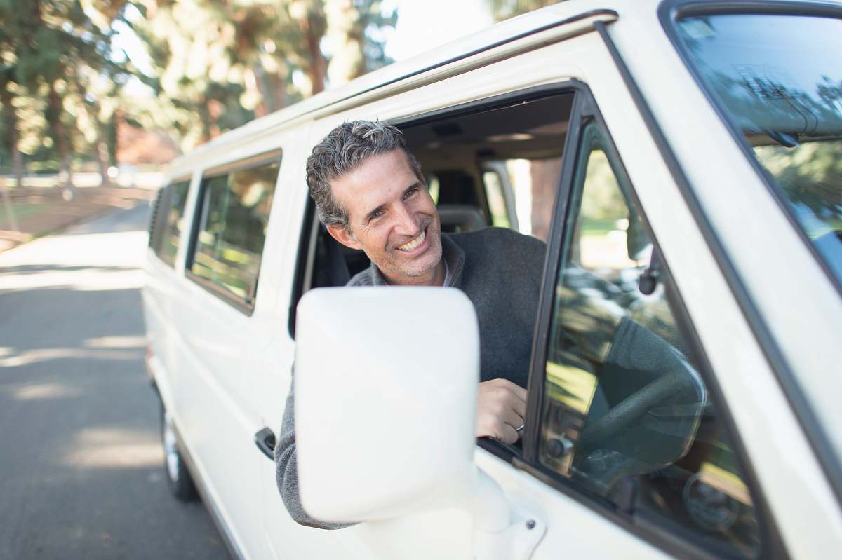 smile man in gray sweater leaning on van window car