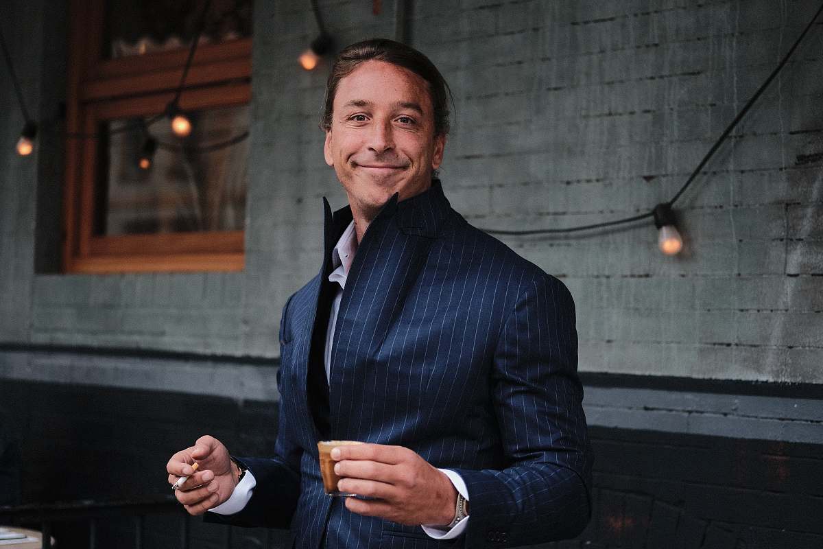 people man wearing black suit holding brown mug near black string lights human