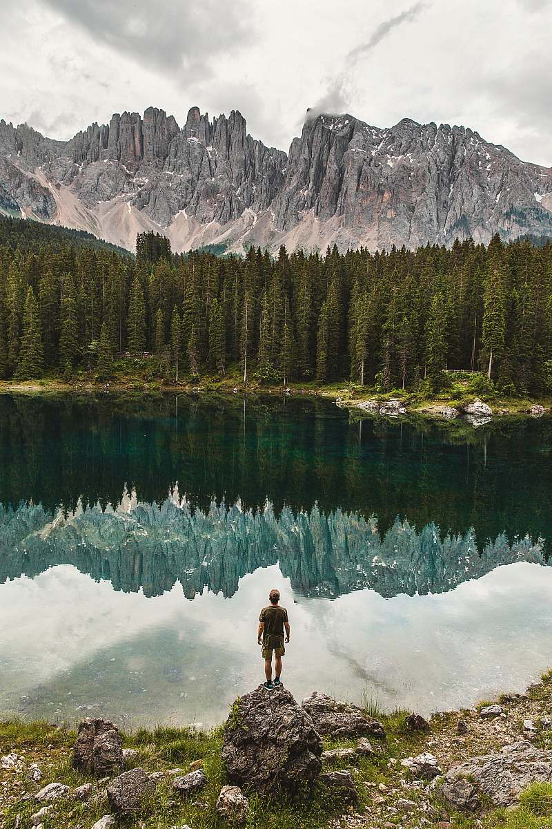 human person standing on cliff in front of forest water