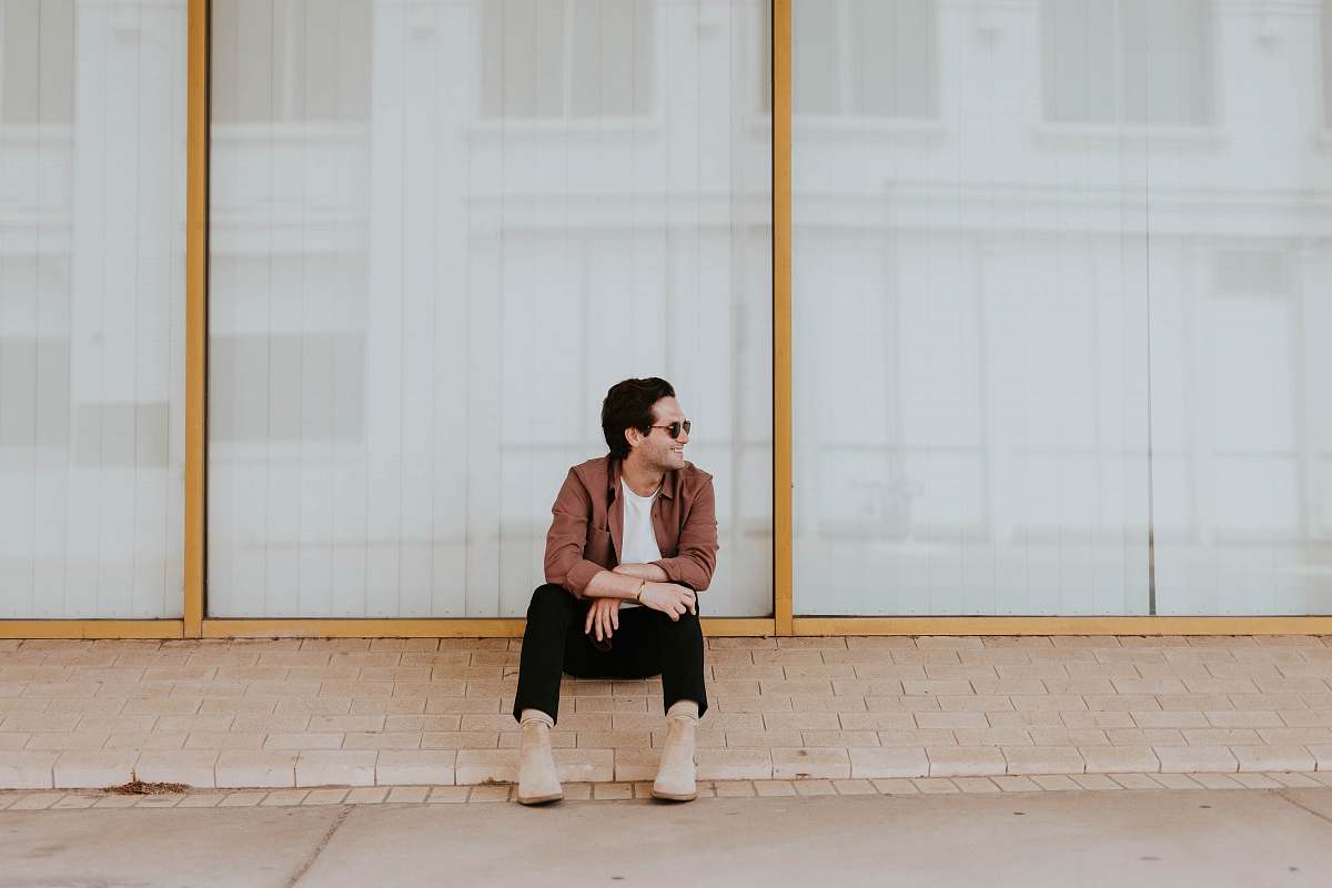 people photo of man sitting on brown bricks against glass wall human