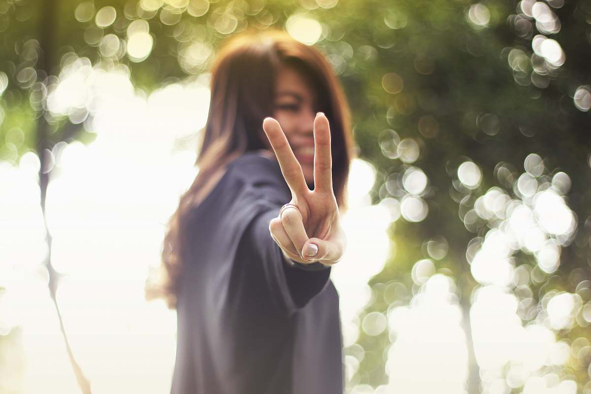 human smiling woman making peace hand sign while standing hand