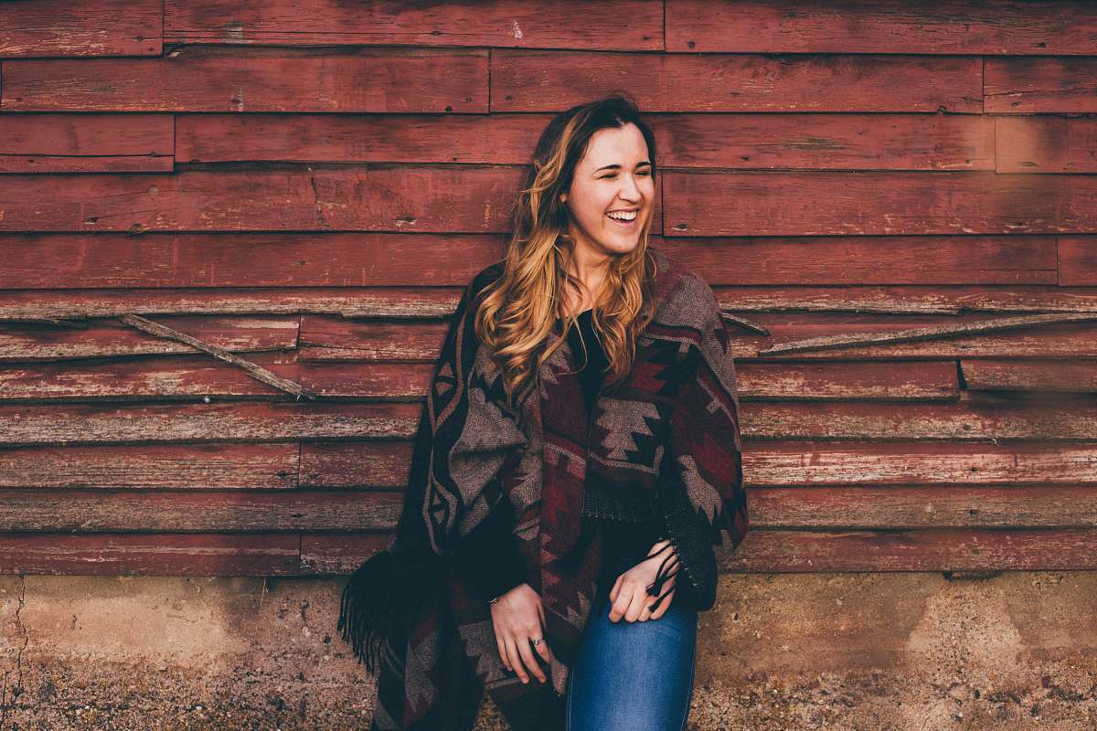 apparel smiling woman wearing brown and black poncho leaning on wall clothing