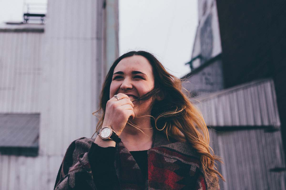 apparel woman standing while laughing and biting her finger clothing