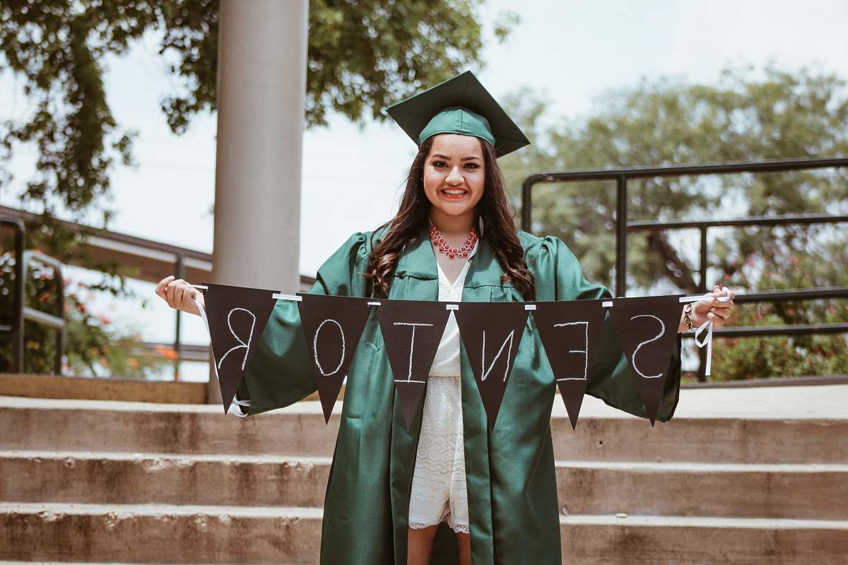 girl woman wearing green academic dress holding black seniors-printed buntings graduation