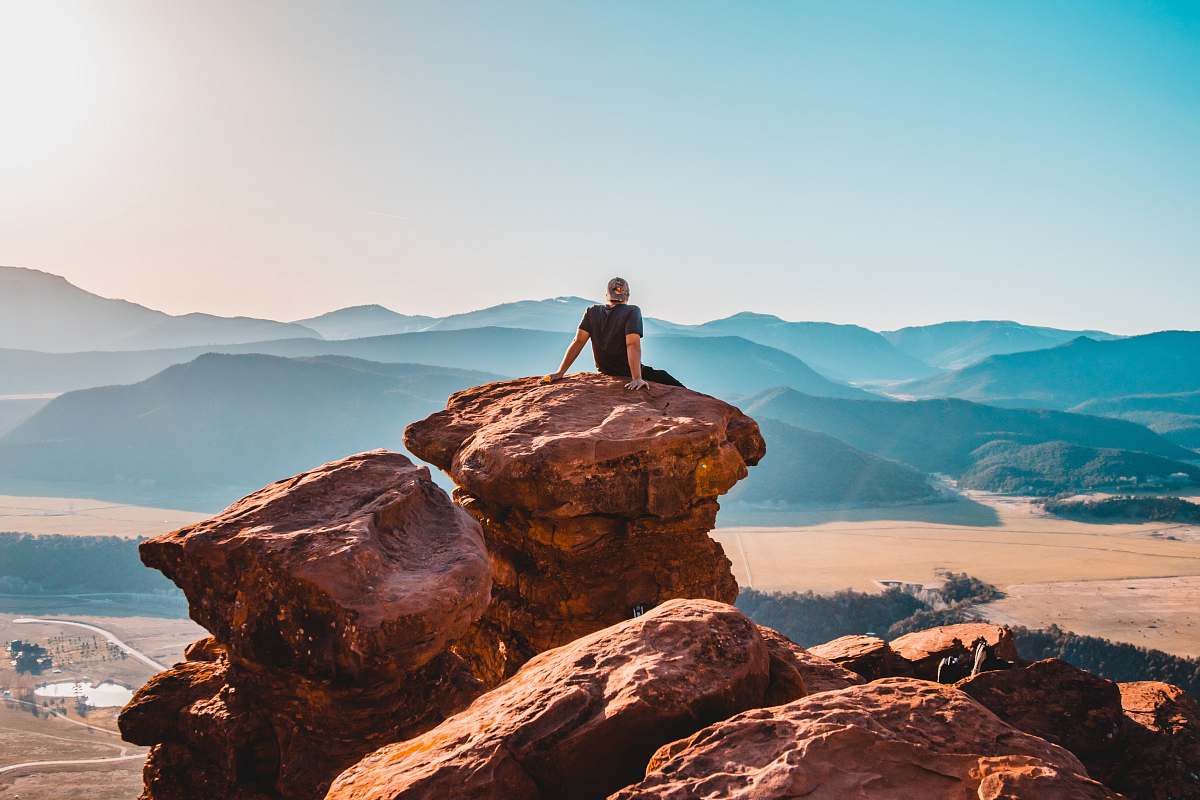 sitting man sitting on rock formation mountains