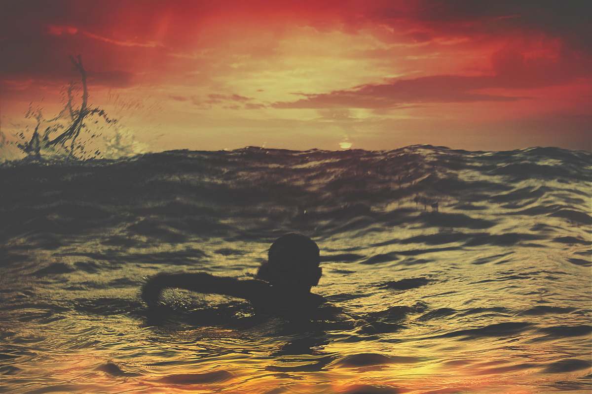 sunset person swimming on body of water under red and orange sky sunrise