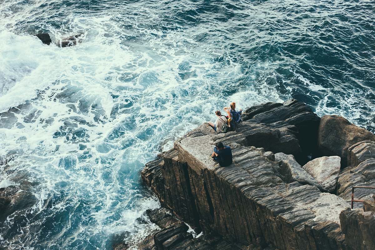 sea people sitting on rock formation on seashore coast