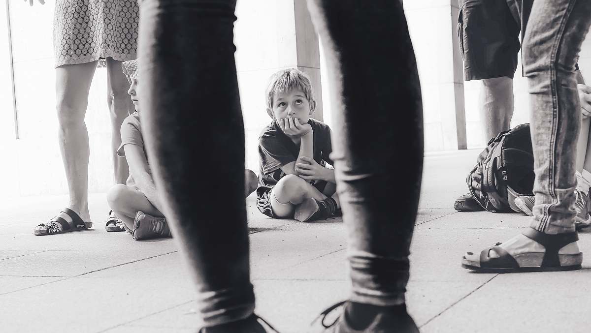 person grayscale photography of boy sitting on the floor watching the person in front of him people