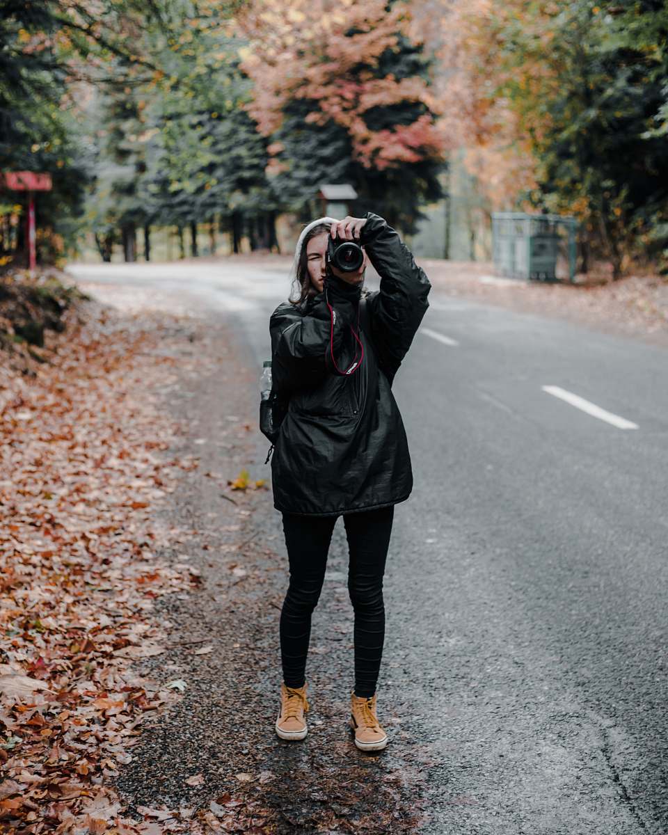 clothing man holding camera standing on road footwear
