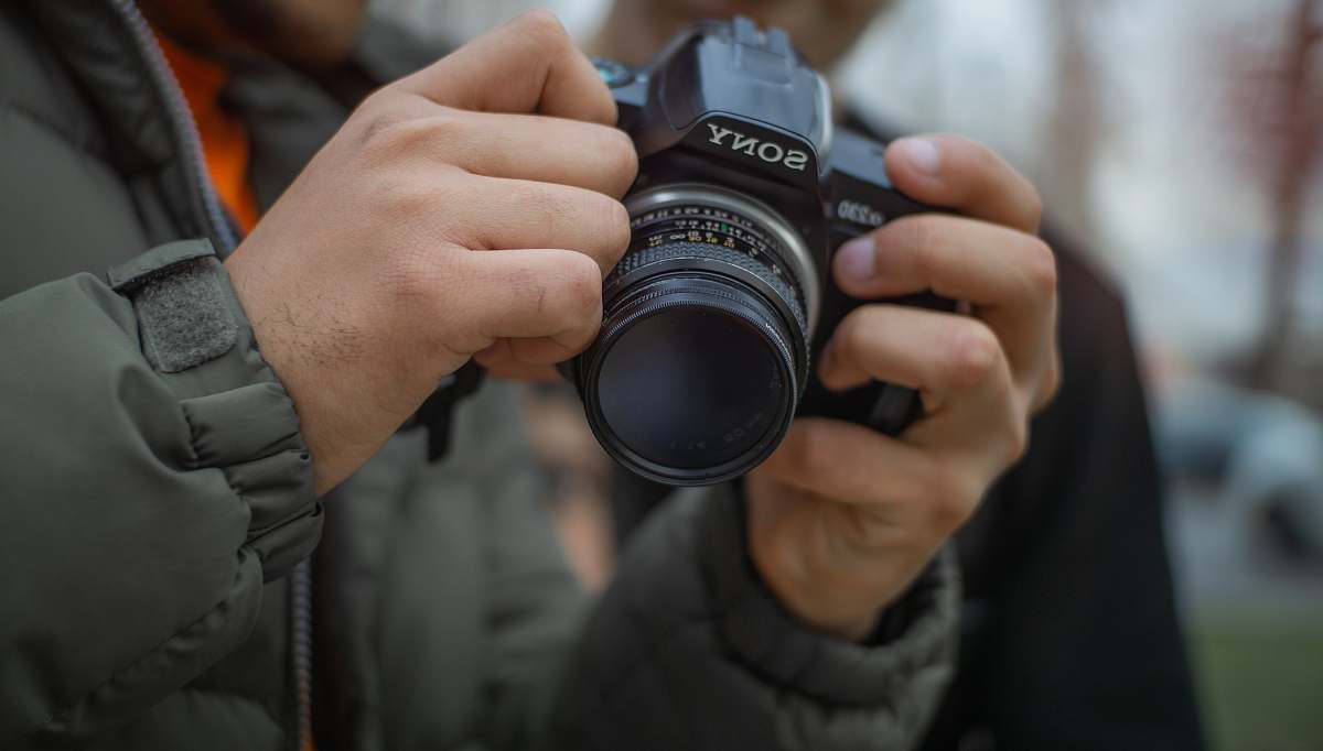 person man in grey jacket holding Sony DSLR camera human