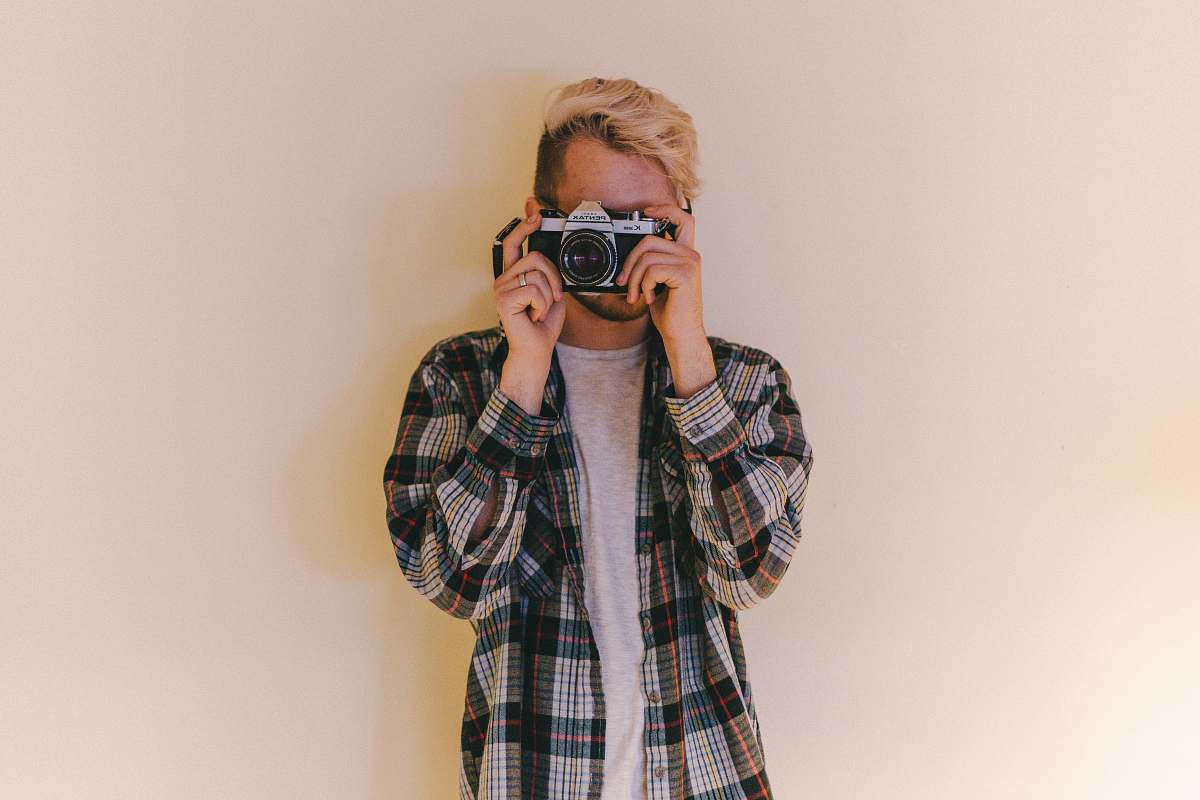 human man wearing black, gray, and brown plaid collared button-up long-sleeved shirt standing while using camera person