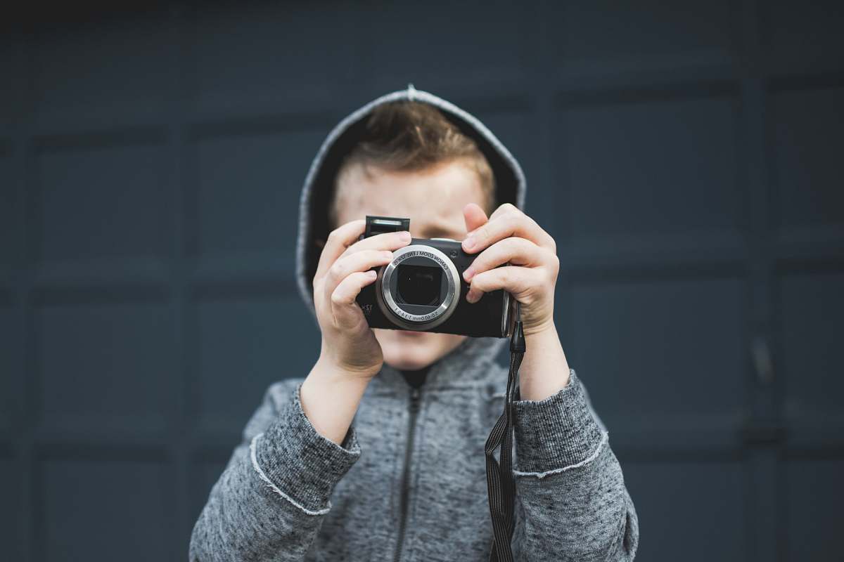 human person in grey hoodie holding up camera over face person