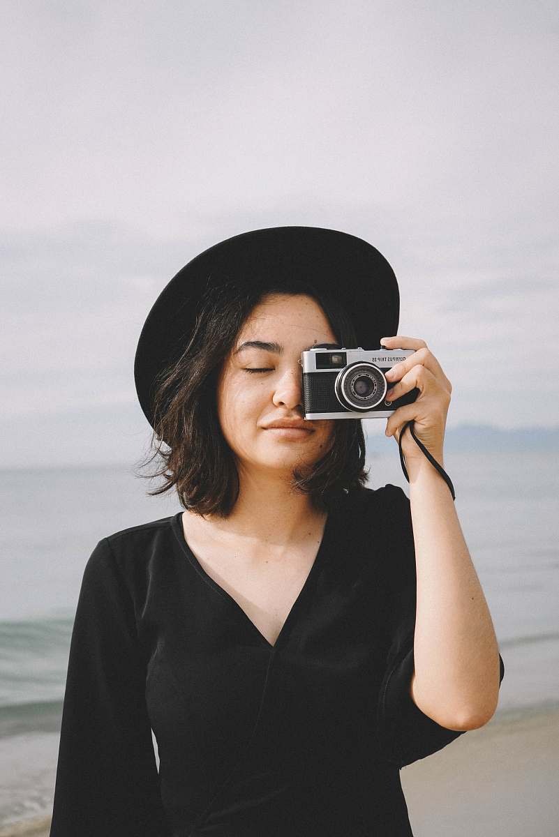 human woman holds camera near to her right eye at the beach person