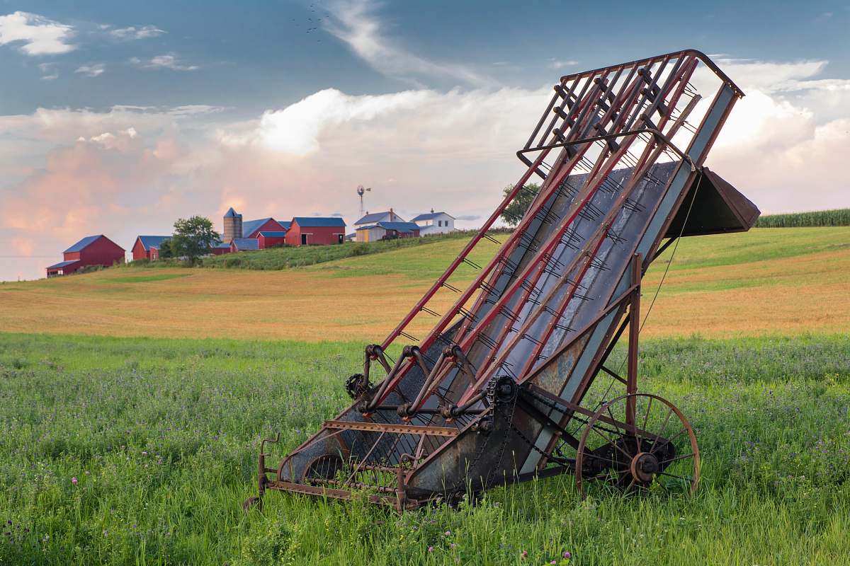 farm grey and red metal harvester machine on green field barn