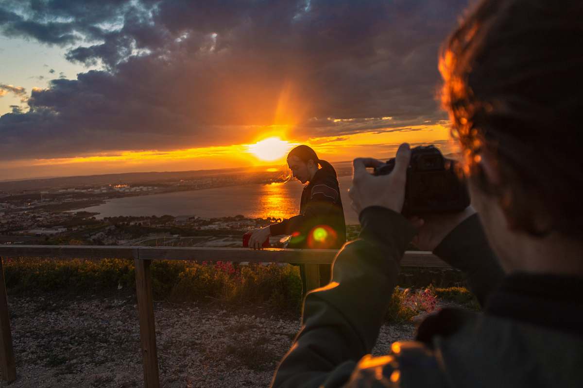 light man taking photo of man beside railing under gray and orange cloudy sky with sun nature