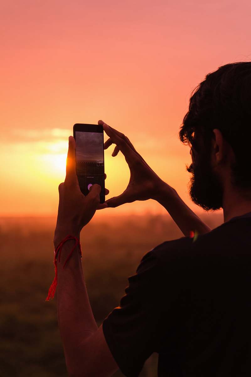 person man holding smartphone on high ground during golden hour outdoors