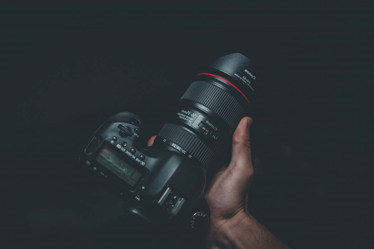 photography person holding black Canon DSLR camera grey