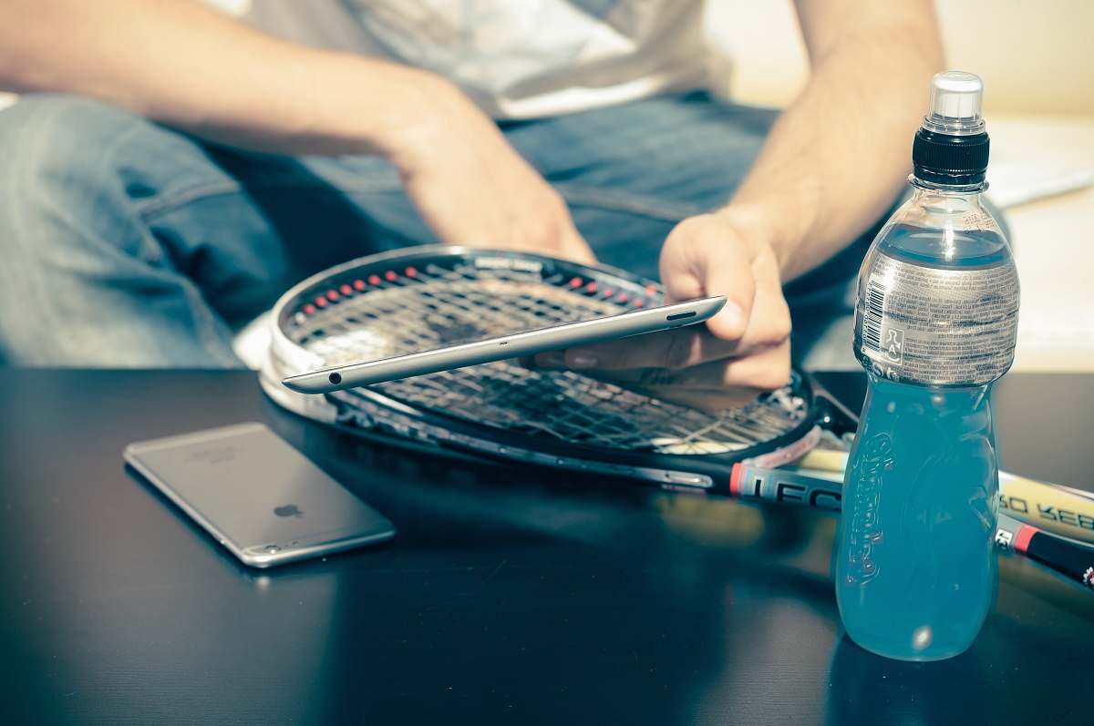 person person sitting while using iPhone 8 and tennis racket beside energy drink bottle cell phone